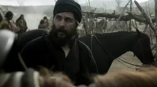 assets/taylor-kitsch-s-isaac-looking-up-at-someone-on-a-horse-in-american-primeval.jpeg