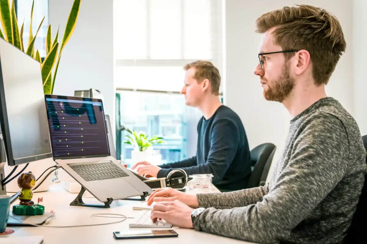 Man-and-his-coworker-both-sitting-at-an-office-desk-doing-work-on-PC