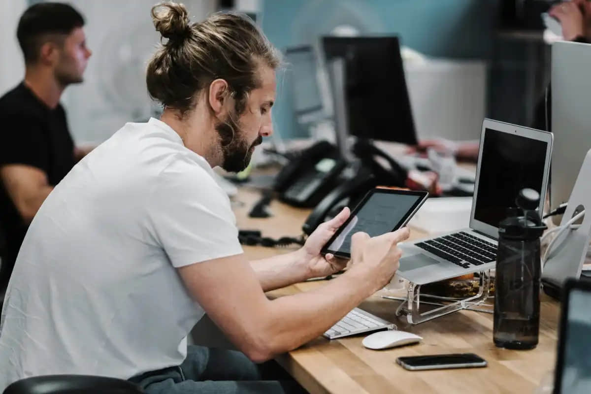Man-with-bun-sitting-in-office-chair-slouched-over-desk-while-working-on-a-tablet