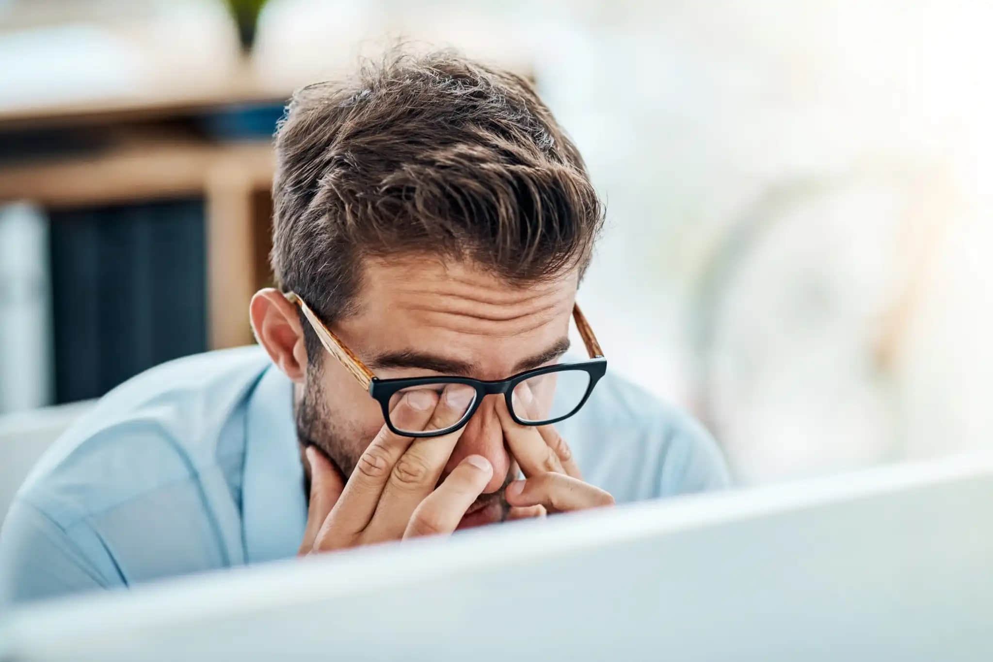 Man-with-glasses-tiredly-rubbing-eyes-while-working-on-a-laptop-PC-1