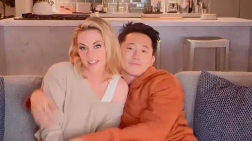 assets/kristen-stewart-and-steven-yeun-sit-and-hug-on-a-couch-in-the-2025-movie-love-me.jpeg