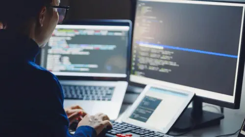 assets/Woman-in-glasses-coding-with-laptop-monitor-and-tablet.jpeg