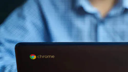 assets/Chrome-logo-on-lid-of-Chromebook-laptop-while-man-in-blue-shirt-uses-it.jpeg