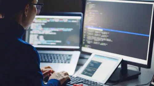 assets/Woman-in-glasses-coding-with-laptop-monitor-and-tablet.jpeg
