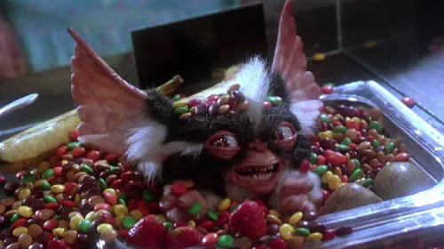 assets/a-gremlin-smiles-from-a-container-of-candy-in-gremlins-2-the-new-batch.jpeg