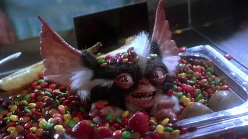 assets/a-gremlin-smiles-from-a-container-of-candy-in-gremlins-2-the-new-batch.jpeg