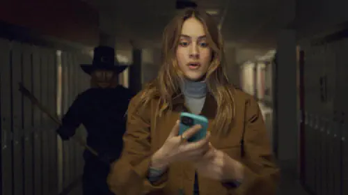 assets/a-girl-looking-at-a-phone-is-unaware-a-masked-killer-stands-behind-her-in-thanksgiving.jpeg