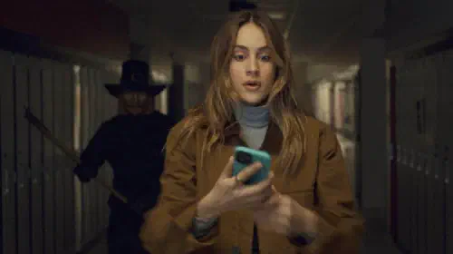assets/a-girl-looking-at-a-phone-is-unaware-a-masked-killer-stands-behind-her-in-thanksgiving.jpeg