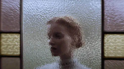 assets/a-woman-stands-behind-a-glass-structure-in-keeper.jpeg