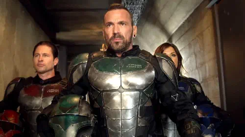 assets/jason-david-frank-as-eric-walking-down-a-hallway-with-two-people-behidn-him-all-in-superhero-suits-in-legend-of-the-white-dragon.jpeg