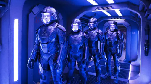 assets/the-expanse-cast-wears-space-suits-as-they-stand-in-a-blue-lit-hallway.jpeg
