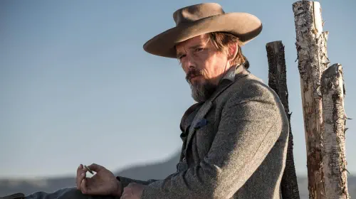 assets/ethan-hawke-wearing-a-cowboy-hat-and-leaning-against-a-post-in-the-magnificent-seven.jpeg