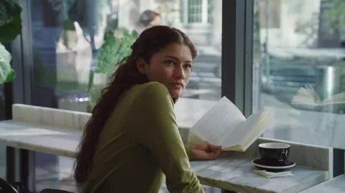 assets/emma-at-a-cafe-holding-a-book-and-looking-over-her-shoulder-in-the-drama.jpeg