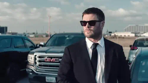 assets/chris-hemsworth-with-sunglasses-on-in-front-of-a-row-of-cars-in-crime-101.jpeg