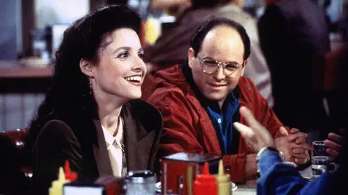 assets/george-and-elaine-sitting-in-monk-s-cafe-in-seinfeld-1.jpeg