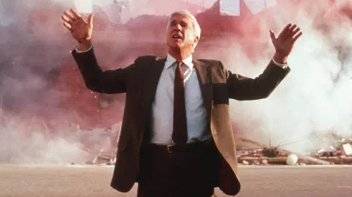 assets/leslie-nielsen-s-frank-standing-in-front-of-an-explosion-with-his-hands-up-in-the-naked-gun.jpeg
