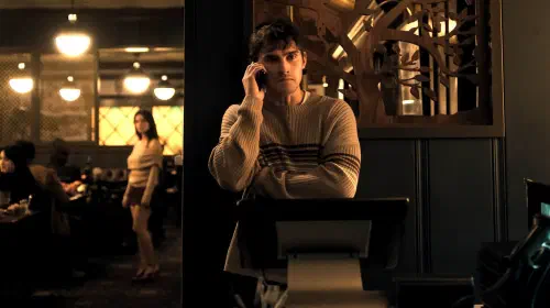 assets/michael-johnston-s-bear-looking-worried-on-the-phone-with-inde-navarrette-s-nikki-standing-creepily-in-the-background-of-the-restaurant-in-obsession.jpeg