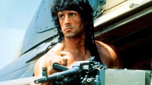 assets/sylvester-stallone-as-john-rambo-leaning-out-of-a-helicopter-with-a-gun-in-rambo-iii.jpeg