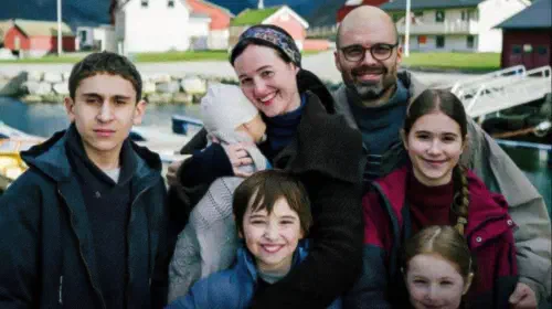 assets/the-gheorghiu-family-posing-together-and-smiling-against-a-norwegian-village-background.jpeg