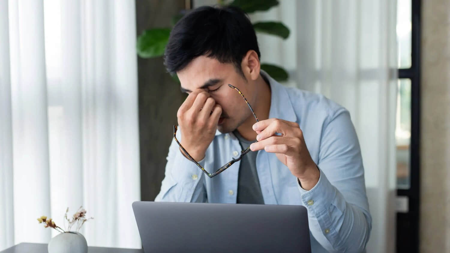 Man-pinching-tired-eyes-with-glasses-off-while-working-at-laptop-on-desk-2.jpeg