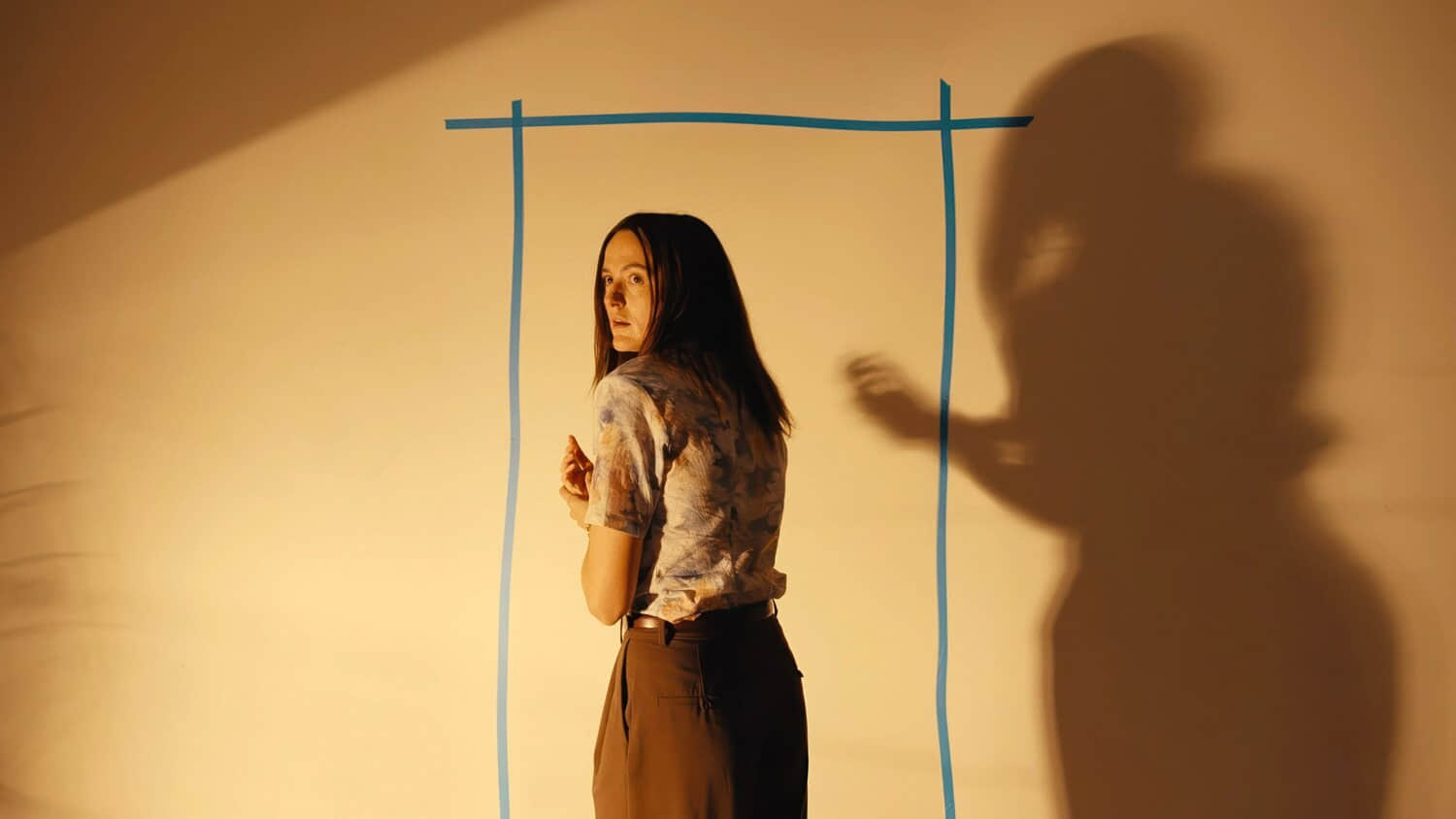 mary-standing-in-front-of-the-blue-tape-outline-of-the-backrooms-door-and-looking-over-her-shoulder.jpeg