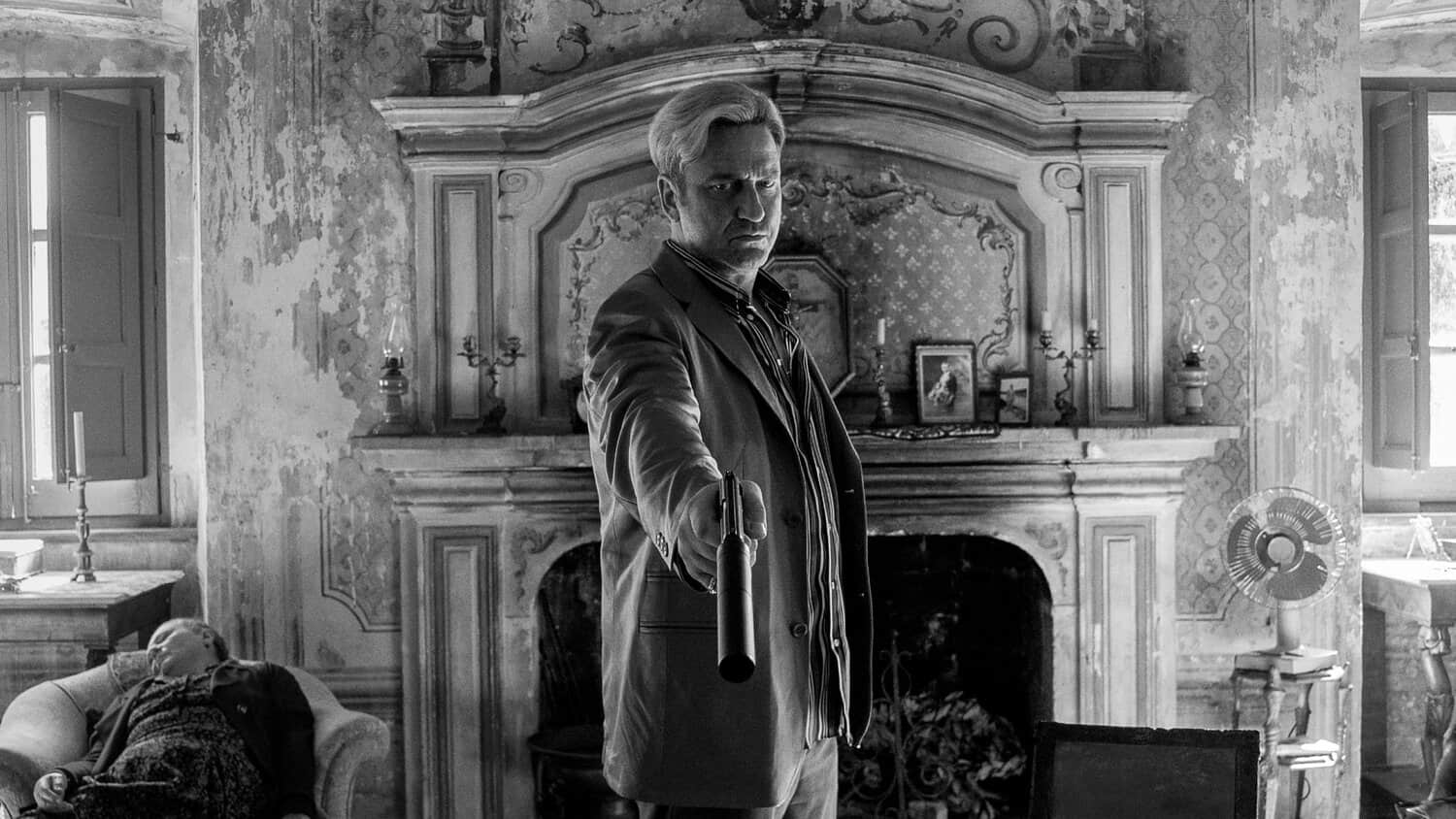 gerard-butler-points-a-gun-at-oscar-isaac-sitting-on-a-couch-in-in-the-hand-of-dante.jpeg