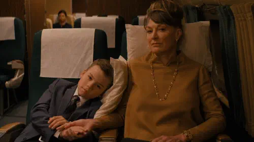 assets/jeff-leaning-on-his-mother-while-seated-in-the-plane-in-propeller-one-way-night-coach.jpeg