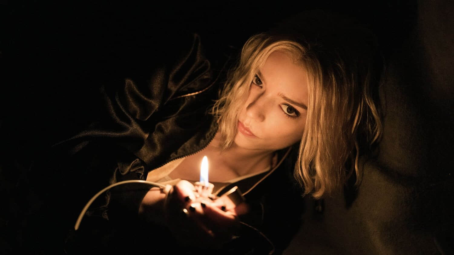 anya-taylor-joy-leans-over-into-the-light-from-a-flame-on-a-lighter-in-apple-tv-series-lucky.jpeg