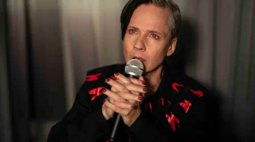 assets/gabe-john-cameron-mitchell-holding-a-microphone-in-shrill-season-2.jpeg