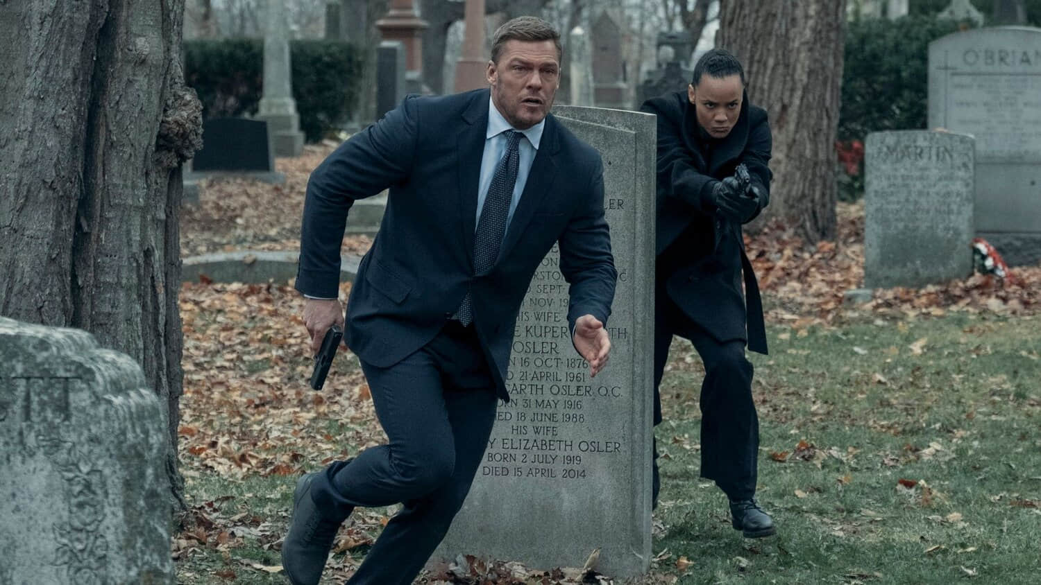 alan-ritchson-and-maria-sten-run-through-a-graveyard-in-reacher.jpeg