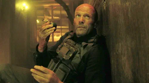 assets/statham-holding-a-grenade-in-a-working-man-2.jpeg